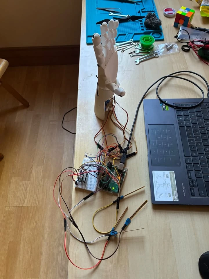 Robotic hand beside Arduino electronics and its wiring on a workbench.